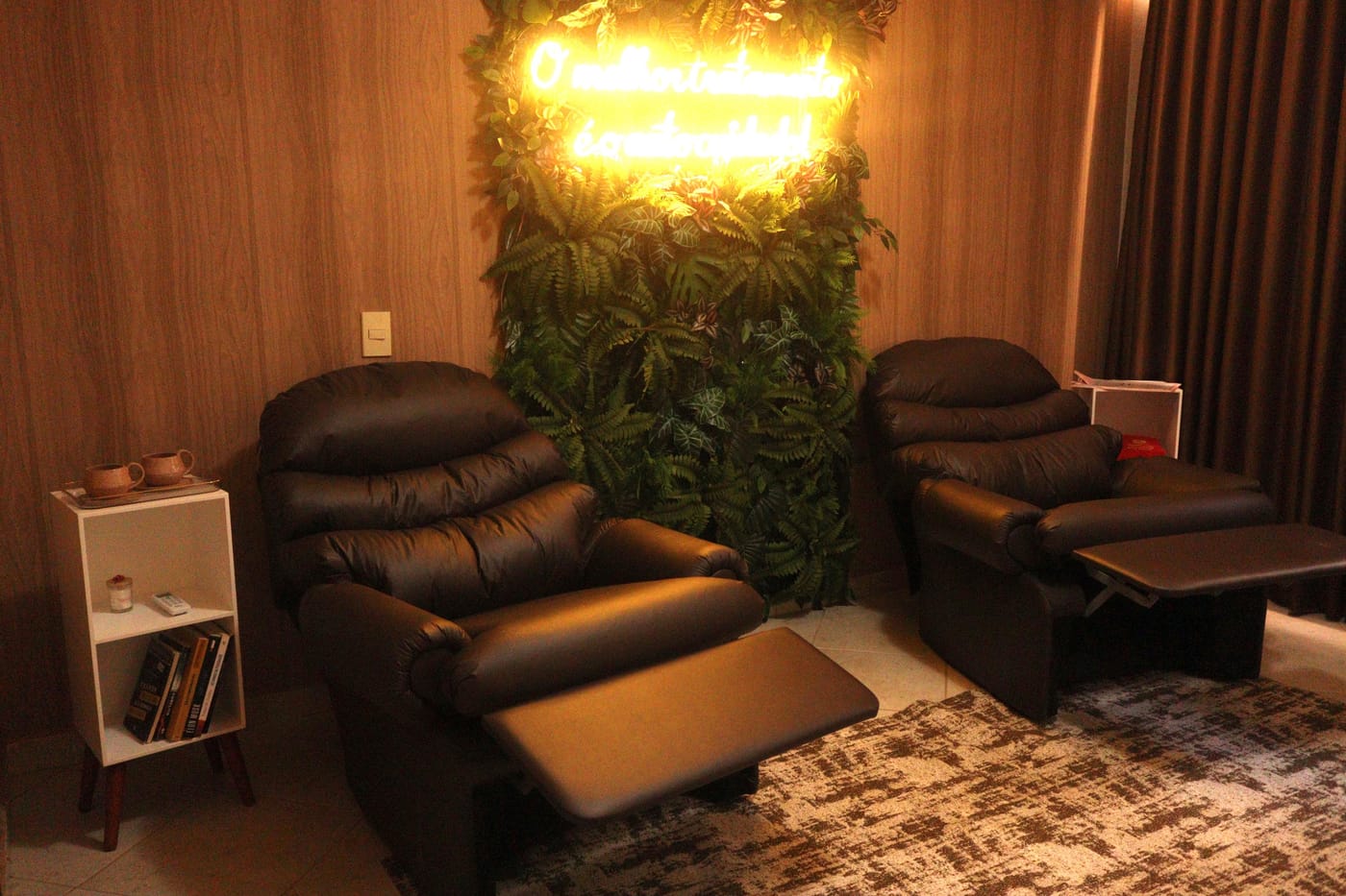 Sala do Morena Café com poltronas reclináveis, parede de folhagem e letreiro luminoso